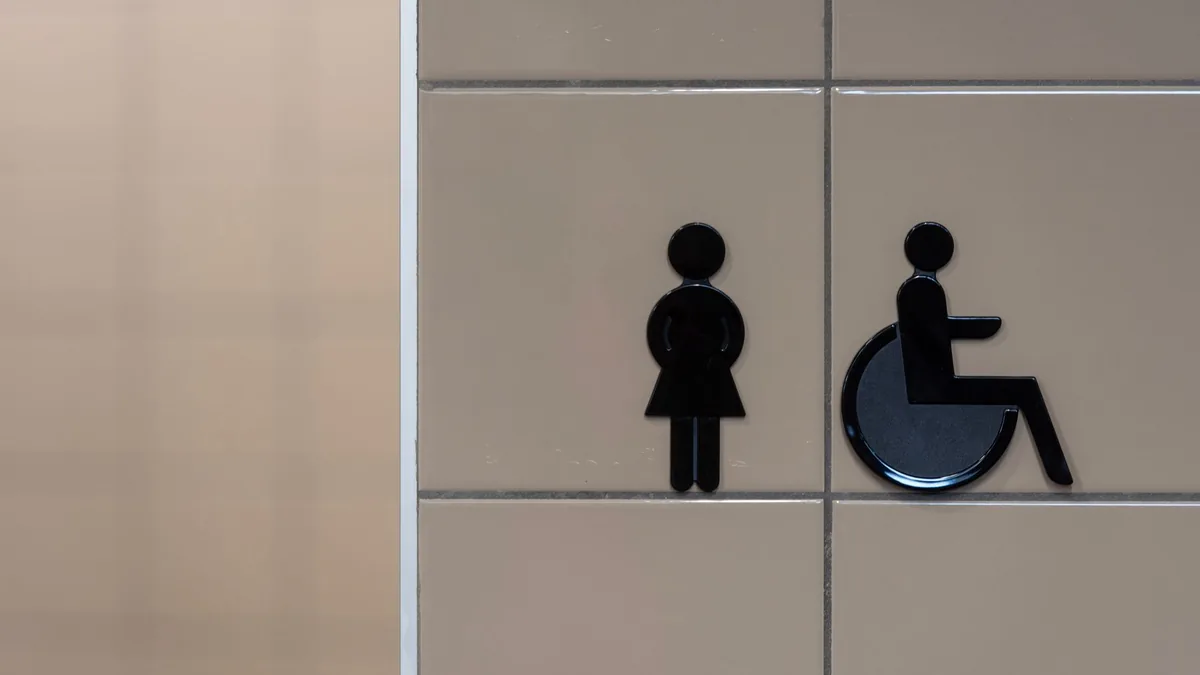 Pictogramas de aseo de mujeres y de aseo adaptado para silla de ruedas sobre una pared de azulejo.