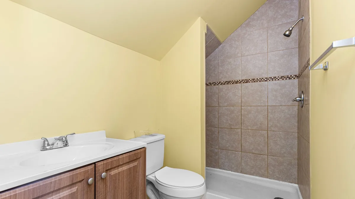Baño pequeño de paredes amarillas con lavabo, inodoro y una ducha con plato blanco y pared de azulejo.