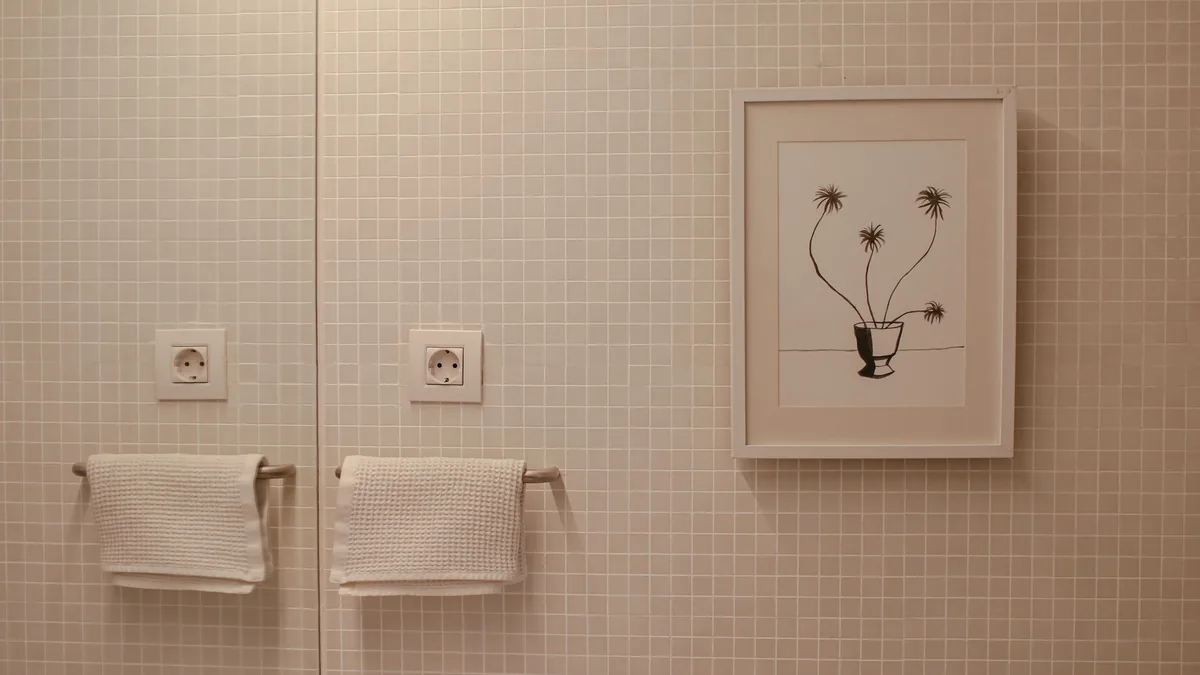 Pared de baño revestida con azulejo de mosaico, con dos toalleros y un cuadro decorativo colgado.